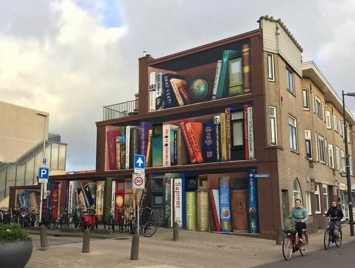 contioutra.com - Artistas holandeses pintam uma prateleira gigante em um prédio de apartamentos com livros favoritos dos moradores